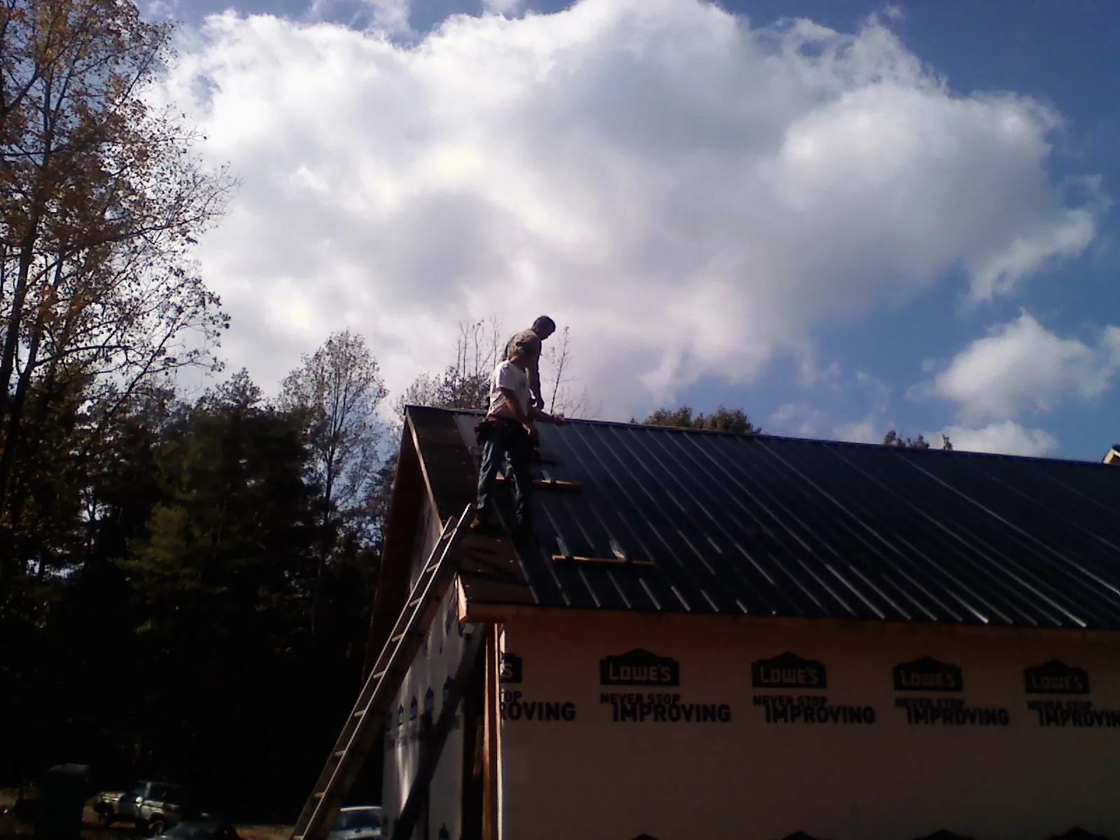 Roofer fastening dark metal panels high against a cloudy sky, from a Roof Inspection job in Woodinville