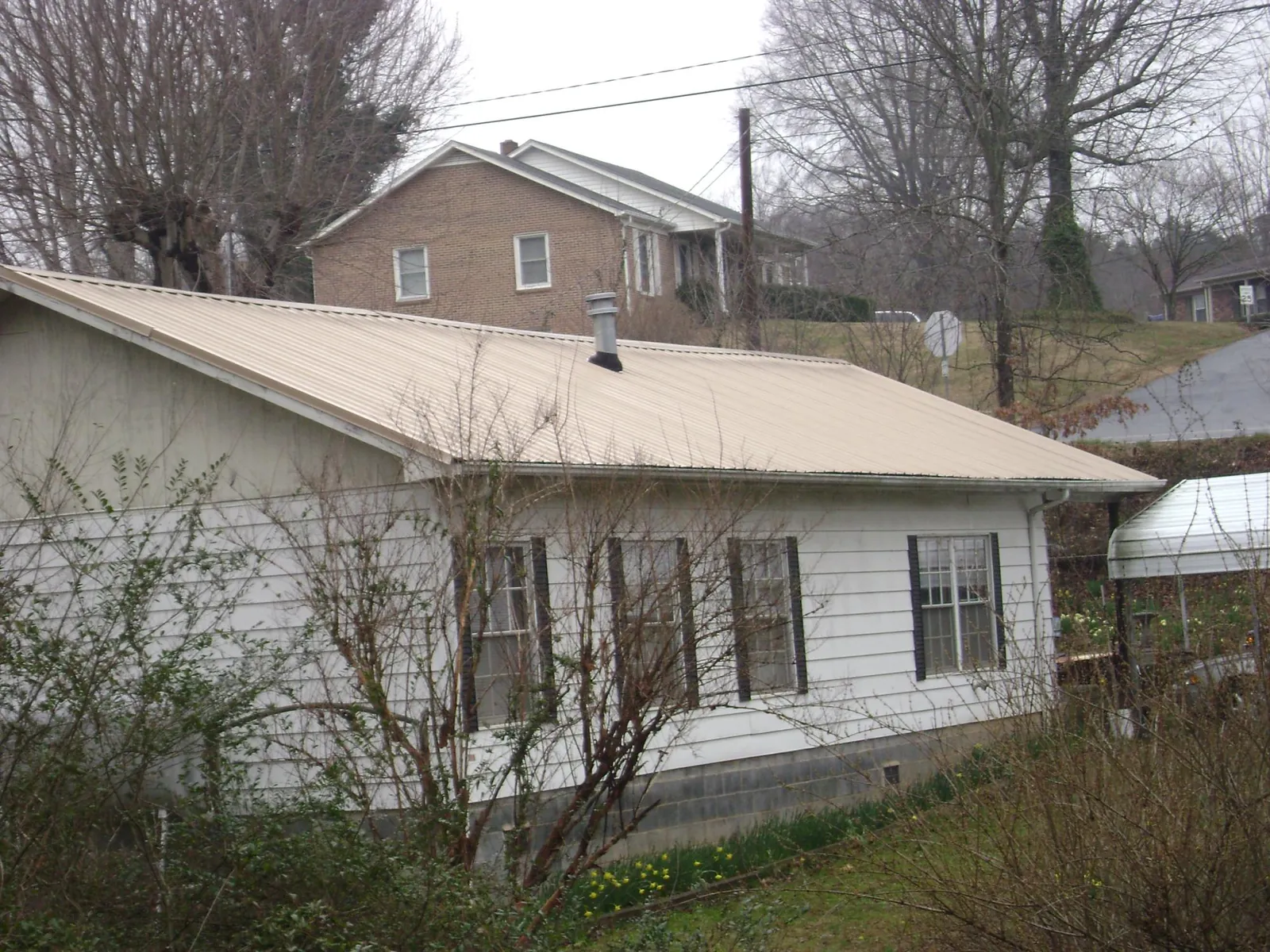 Tan metal roof on a white sided house set into a hillside — Commercial Roofing by Roofing Brothers in Woodinville